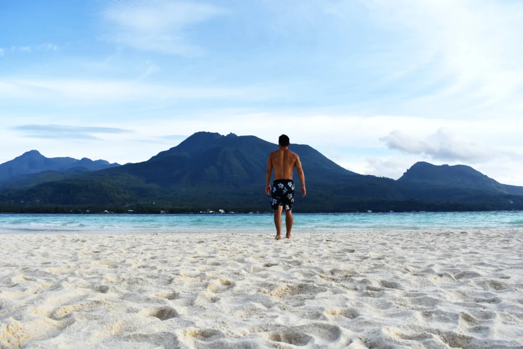 man standing on a white sand of camiguin White Island facing Mt. Hibok-Hibok